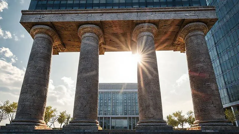 A photorealistic image of four strong, interconnected stone pillars supporting a modern corporate building, with sunlight streaming through the gaps, symbolizing strength, foundation, and transparency. Professional photography, 8K, cinematic lighting, sharp focus, depth of field, shot on a high-end DSLR.