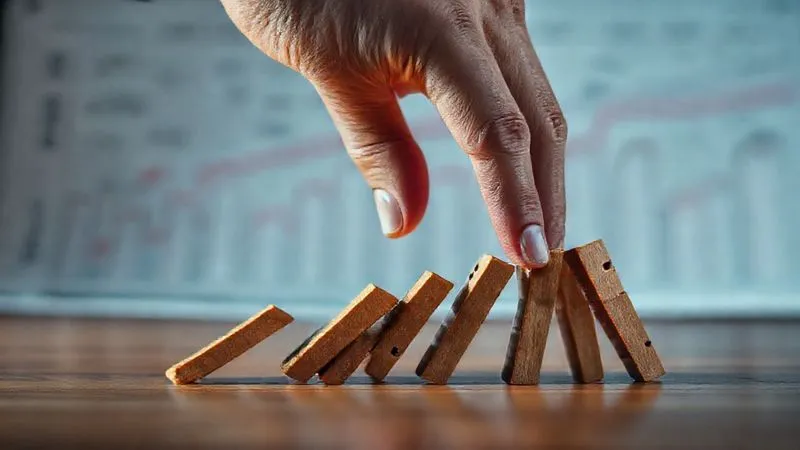 Photorealistic, professional photography, 8K, cinematic lighting, sharp focus, depth of field, shot on a high-end DSLR. A project manager's hand firmly but gently pressing down on a series of falling dominoes, preventing them from toppling further. The background shows a blurry, complex project timeline chart. The scene evokes a sense of immediate control and containment in a chaotic situation. Photorealistic, professional photography, 8K, cinematic lighting, sharp focus, depth of field, shot on a high-end DSLR. A project manager's hand firmly but gently pressing down on a series of falling dominoes, preventing them from toppling further. The background shows a blurry, complex project timeline chart. The scene evokes a sense of immediate control and containment in a chaotic situation.