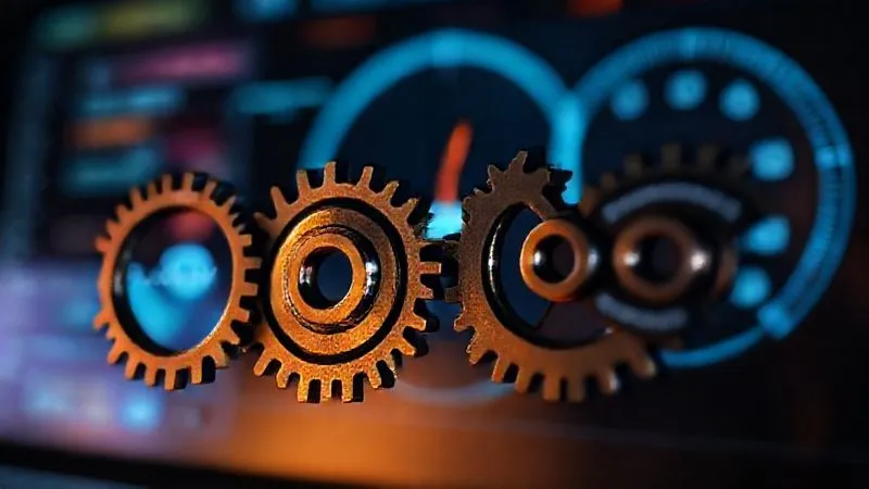 Photorealistic, professional photography, 8K, cinematic lighting, sharp focus, depth of field. A series of interlocking gears, some labeled 'Policy', 'Review', 'Update', and 'Compliance', turning smoothly against a blurred background of a digital dashboard. The lighting is dynamic, highlighting the continuous motion and interconnectedness of the process. The image conveys a systematic and iterative policy management cycle.