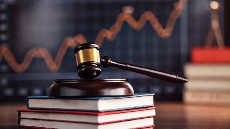 A photorealistic image of a gavel resting on a stack of legal books, with a blurred backdrop of a financial graph showing upward trends, symbolizing justice and monetary recovery. The scene is illuminated with dramatic, high-contrast lighting, emphasizing the gavel. Sharp focus on the gavel and books, with a shallow depth of field. 8K hyper-detailed, professional photography, shot on a high-end DSLR.
